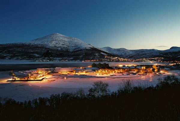 Elkem Saltens smelteverk lyser opp landskapet ved fjorden, med fjell i bakgrunnen.