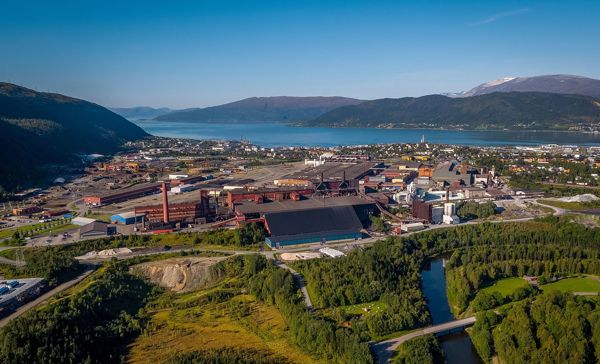 Flyfoto av Elkem Rana med industriområdet, fjell og fjord i bakgrunnen.